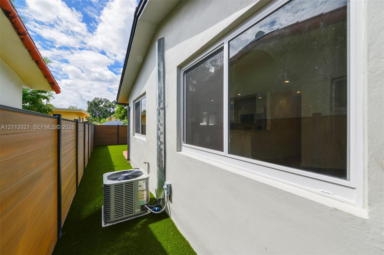 Exterior side yard featuring horizontal composite privacy fencing, synthetic turf, a stucco facade, and aluminum-framed windows