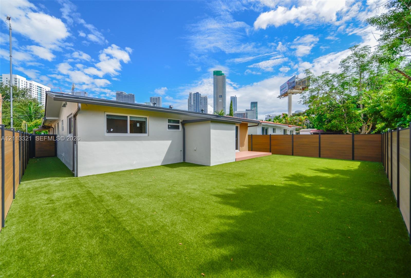 Rear exterior featuring synthetic turf lawn, horizontal wood-finish privacy fencing, and a concrete patio