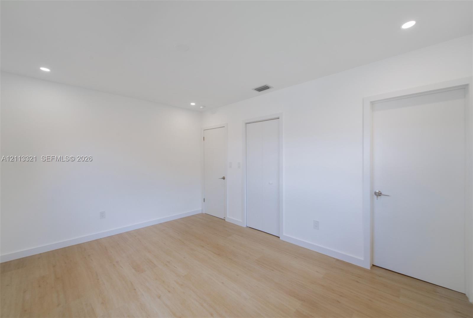 Neutral-toned space featuring wood-finish flooring, recessed lighting, and multiple interior doors with brushed nickel hardware