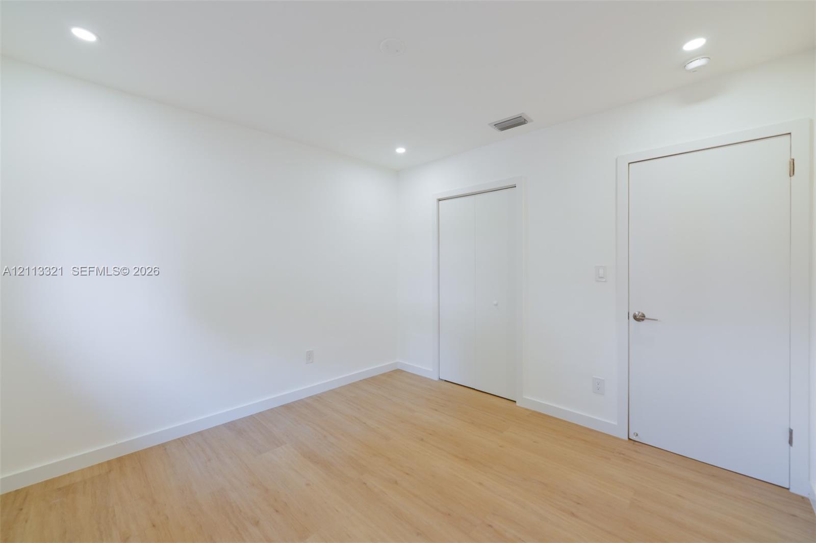 Interior space featuring wood-finish flooring, recessed lighting, and white walls, including a standard interior door and a double-panel closet door
