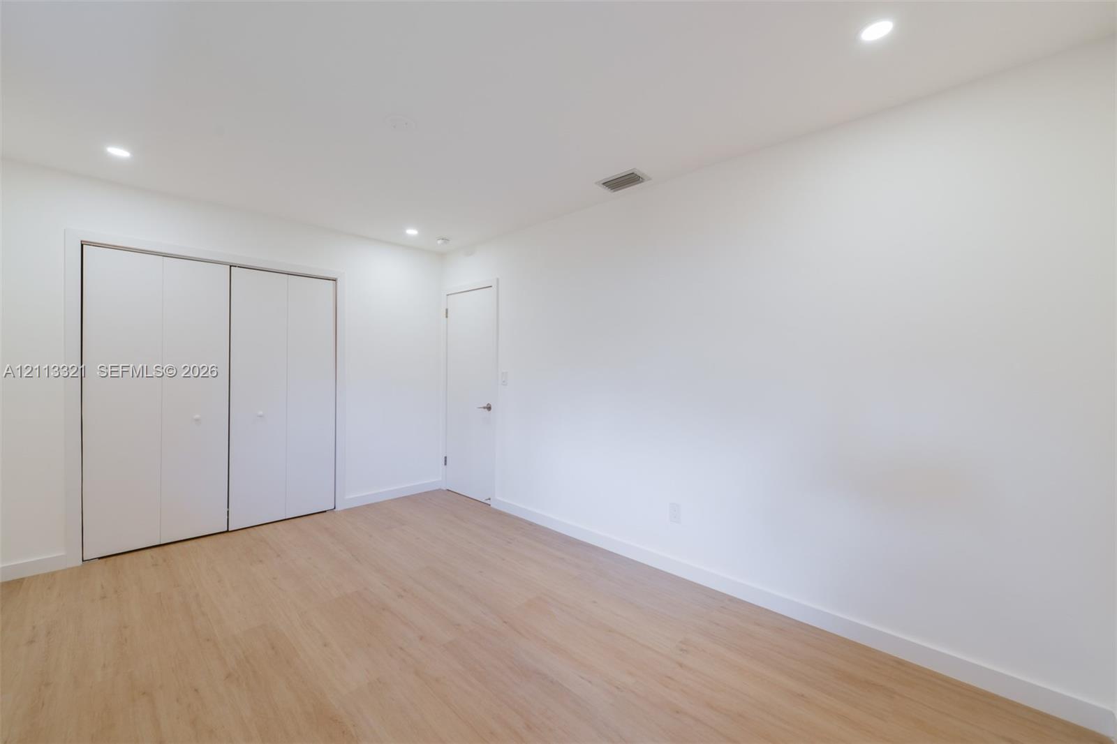 Neutral-toned wood-finish flooring, recessed lighting, and white dual-panel closet doors
