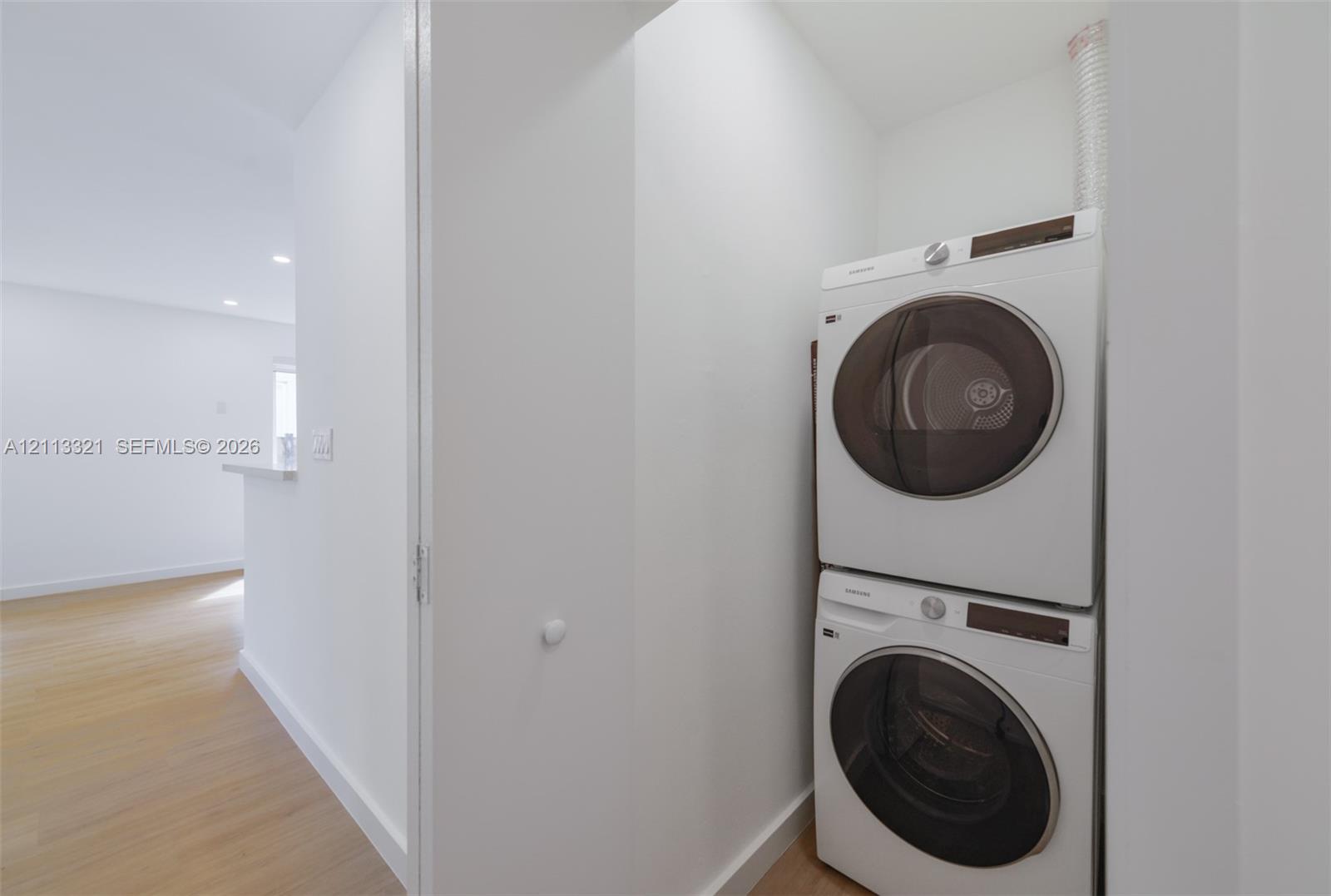 Stacked laundry center featuring white front-load appliances and wood-finish flooring