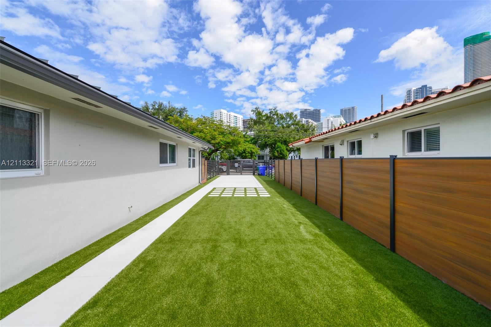Exterior side yard featuring synthetic turf, concrete paver path, wood-finish privacy fencing, and metal gate