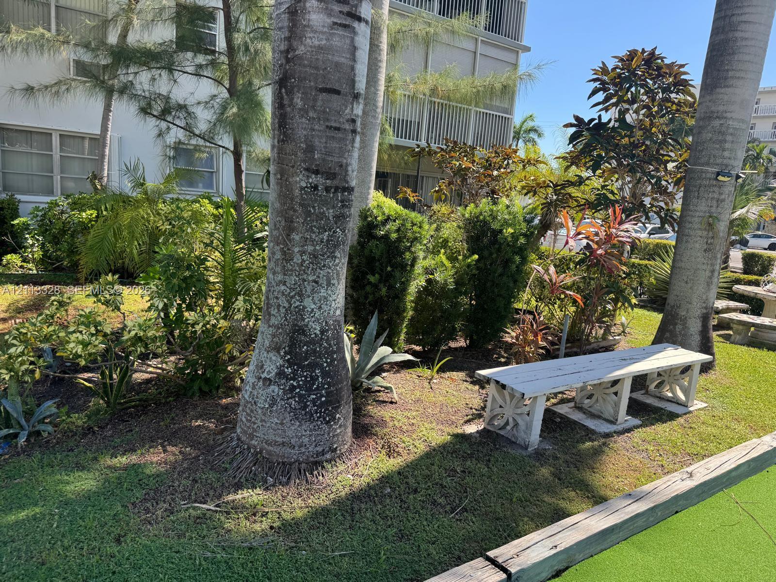 Landscaped grounds featuring mature palm trees, manicured shrubbery, and decorative concrete benches
