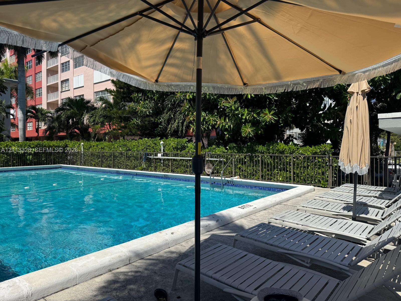 In-ground swimming pool featuring a tile border, concrete decking, and metal perimeter fencing surrounded by mature greenery