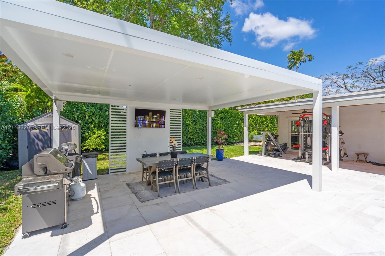 Covered outdoor patio featuring a flat-roof structure with recessed lighting, light-toned stone tile flooring, and vertical slatted privacy screening