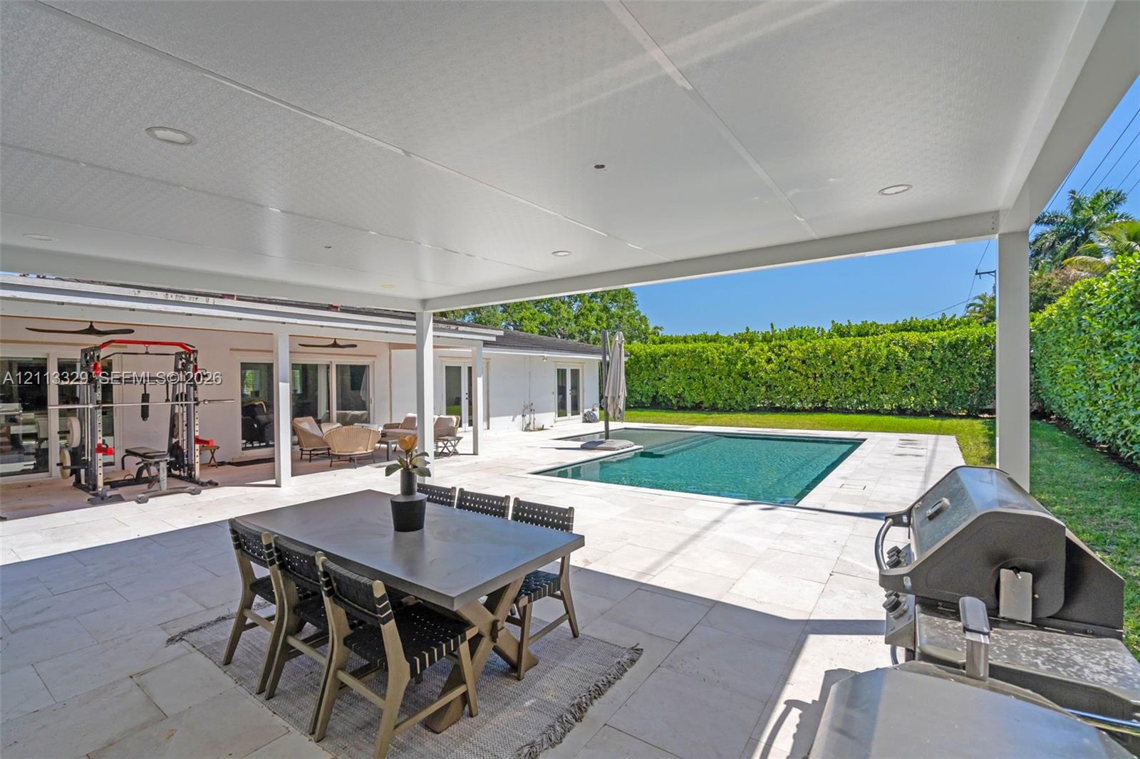 Covered patio featuring recessed lighting, light-toned stone flooring, an inground swimming pool, and a privacy hedge