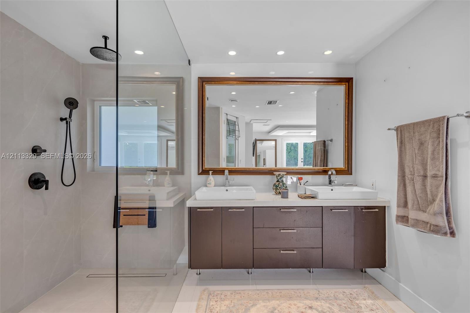 Double vanity with rectangular vessel sinks, quartz countertop, glass-enclosed shower featuring a rainfall showerhead, and a large framed mirror