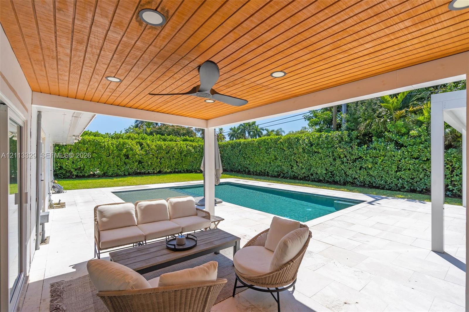 Covered patio featuring a wood-plank ceiling, recessed lighting, and a ceiling fan, opening to a stone-paved pool deck and in-ground swimming pool