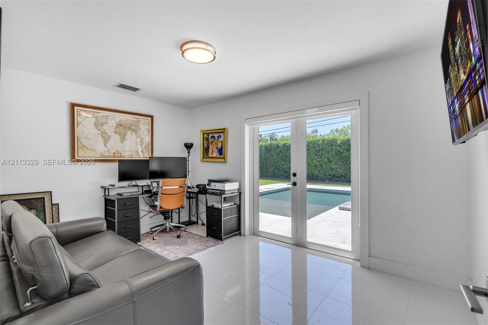 Room featuring white tile flooring, flush-mount lighting, and glass-paneled double doors providing outdoor access to an in-ground pool area