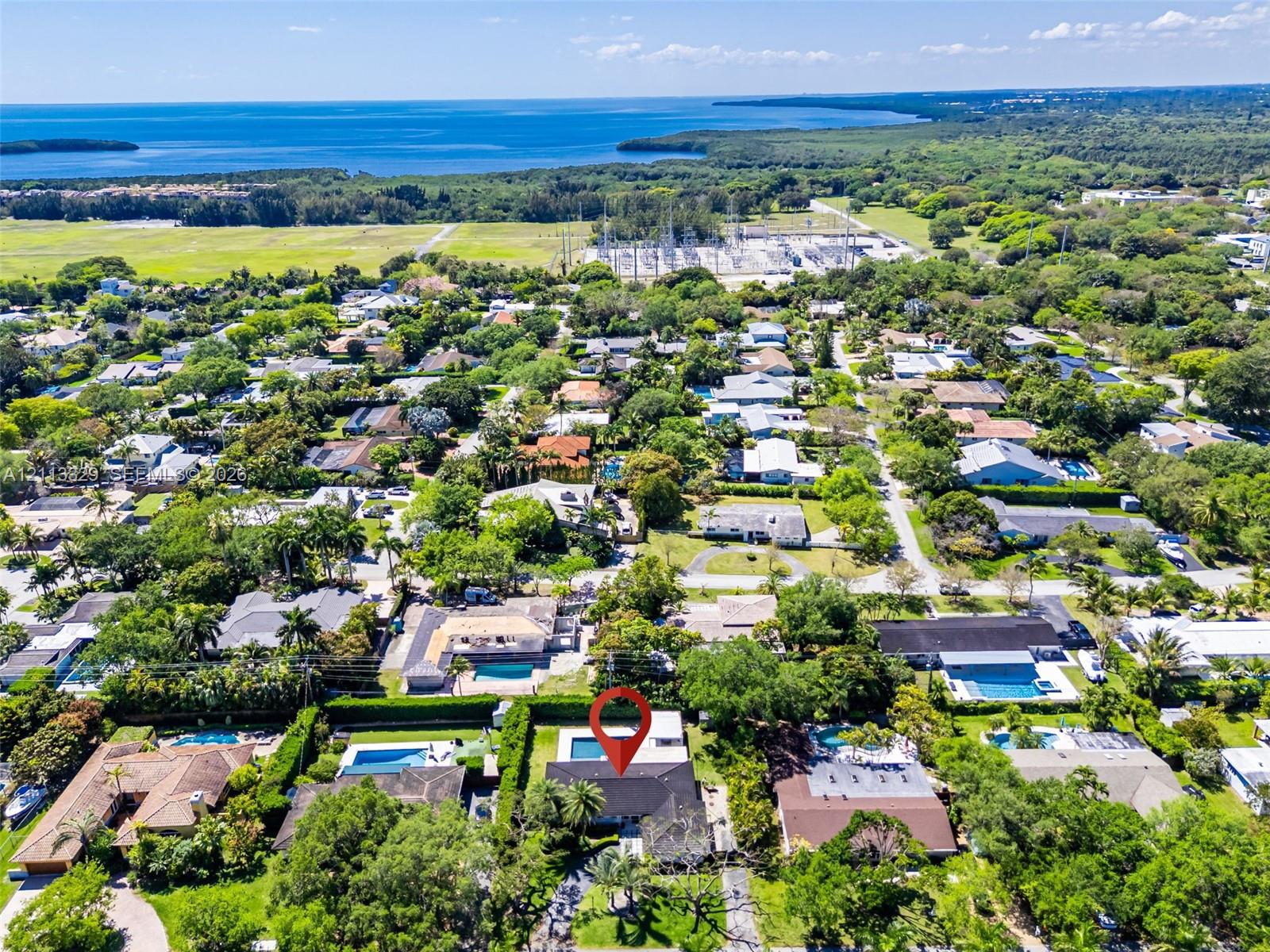 Aerial perspective showcasing a residential property with a swimming pool and mature landscaping, positioned within a coastal environment
