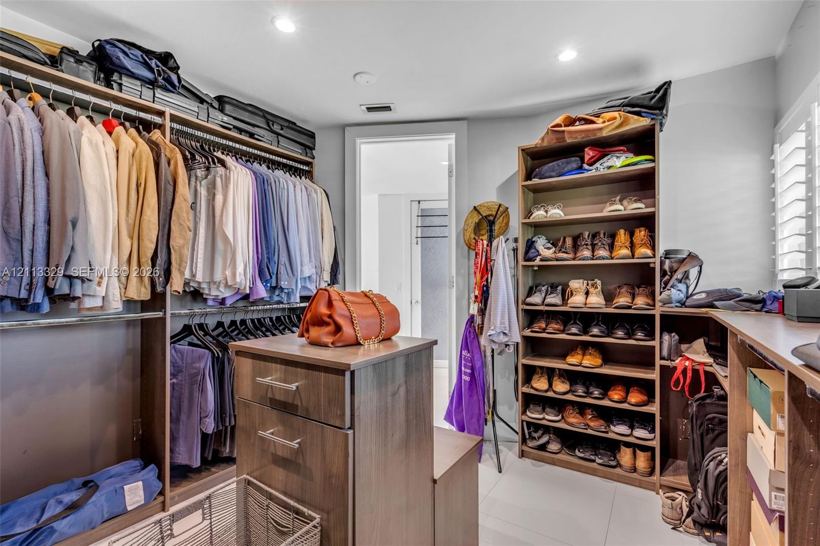 Walk-in storage space featuring built-in wood-finish shelving, an integrated center island with drawers, double-tier clothing rods, and recessed lighting