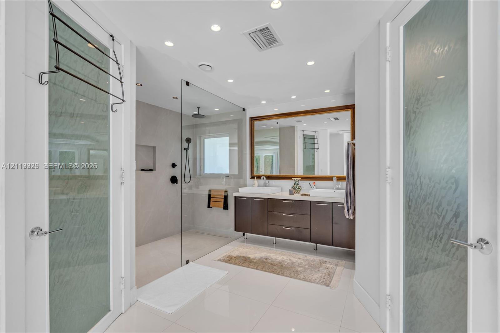 Floating dark-wood cabinetry with dual rectangular vessel sinks, walk-in glass-enclosed shower featuring matte black fixtures, and large framed wall mirror