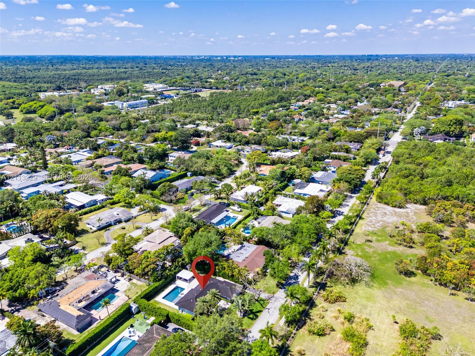 Aerial perspective of a property featuring a swimming pool, covered outdoor area, mature perimeter landscaping, and shingle-style roof