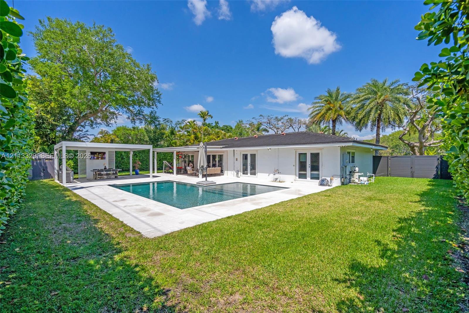 Backyard featuring a swimming pool, concrete patio, covered pergola, expansive lawn, and perimeter privacy hedges