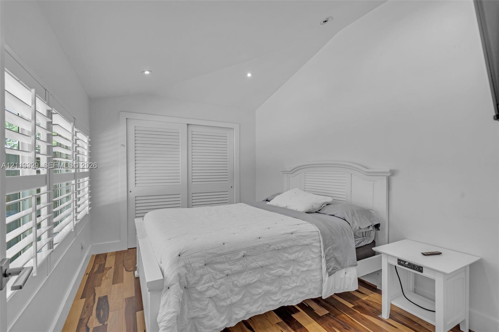 Vaulted ceiling with recessed lighting, wood-finish flooring, and white louvered-style closet doors