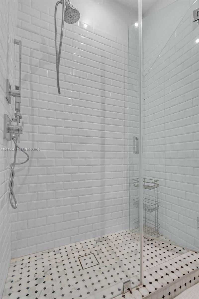 Walk-in shower featuring white subway tile walls, geometric patterned tile flooring, a frameless glass door, and polished chrome plumbing fixtures