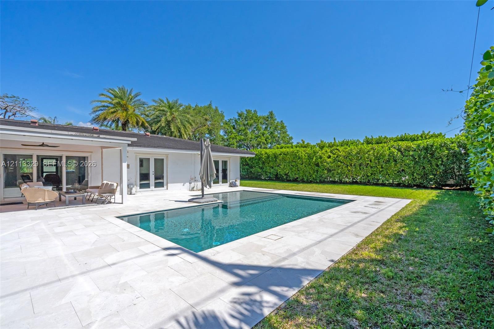 Rectangular swimming pool featuring a stone-paver deck, covered patio, and manicured perimeter landscaping