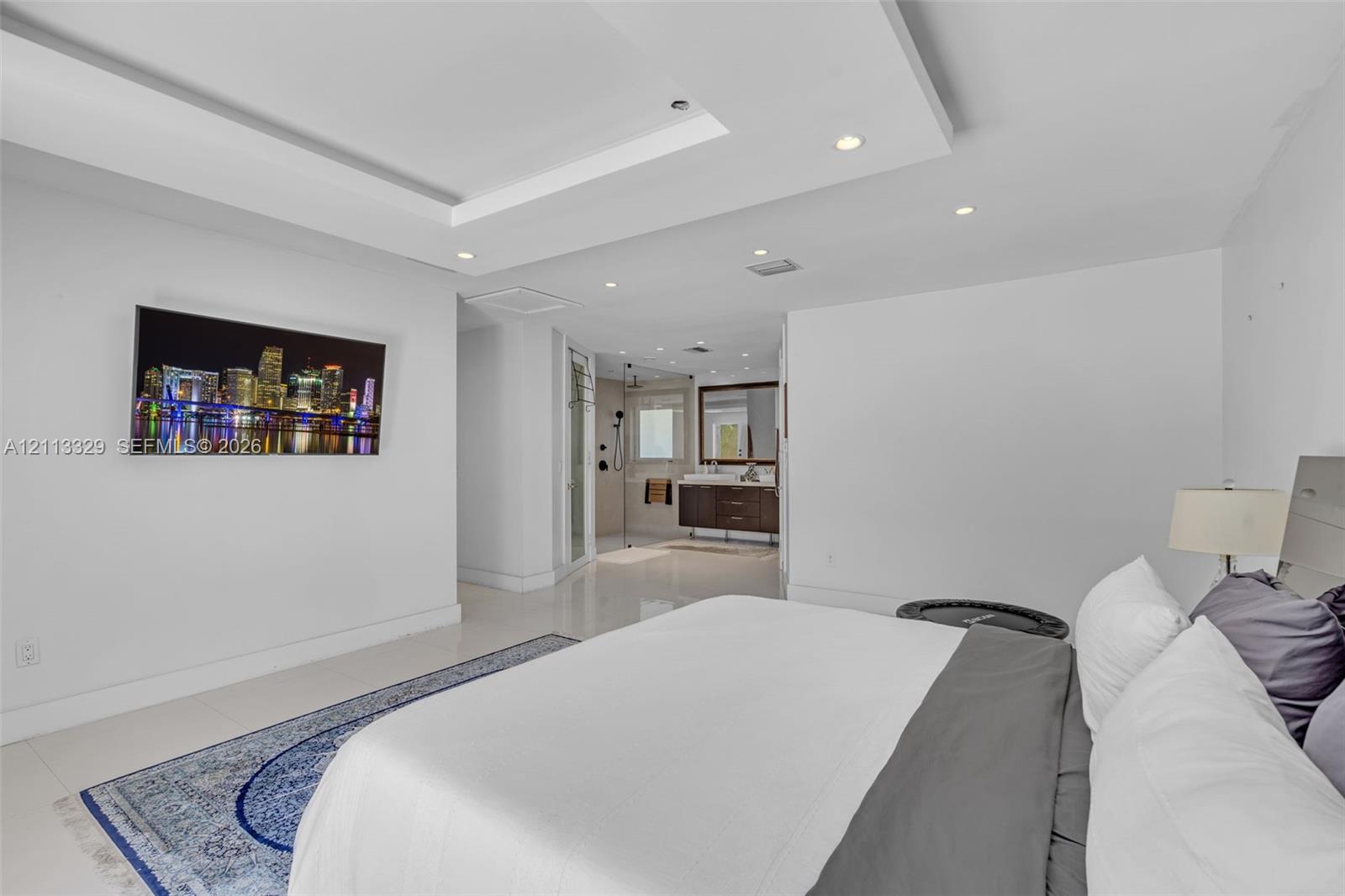 Tray ceiling with recessed lighting, large-format tile flooring, and en-suite bathroom featuring a dark wood vanity