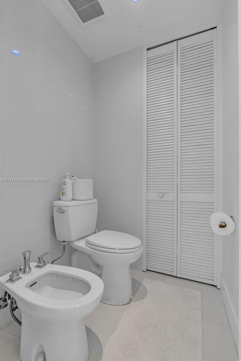 Restroom featuring a floor-mounted bidet with polished chrome fixtures, a standard-height toilet, and floor-to-ceiling louvered-style closet doors