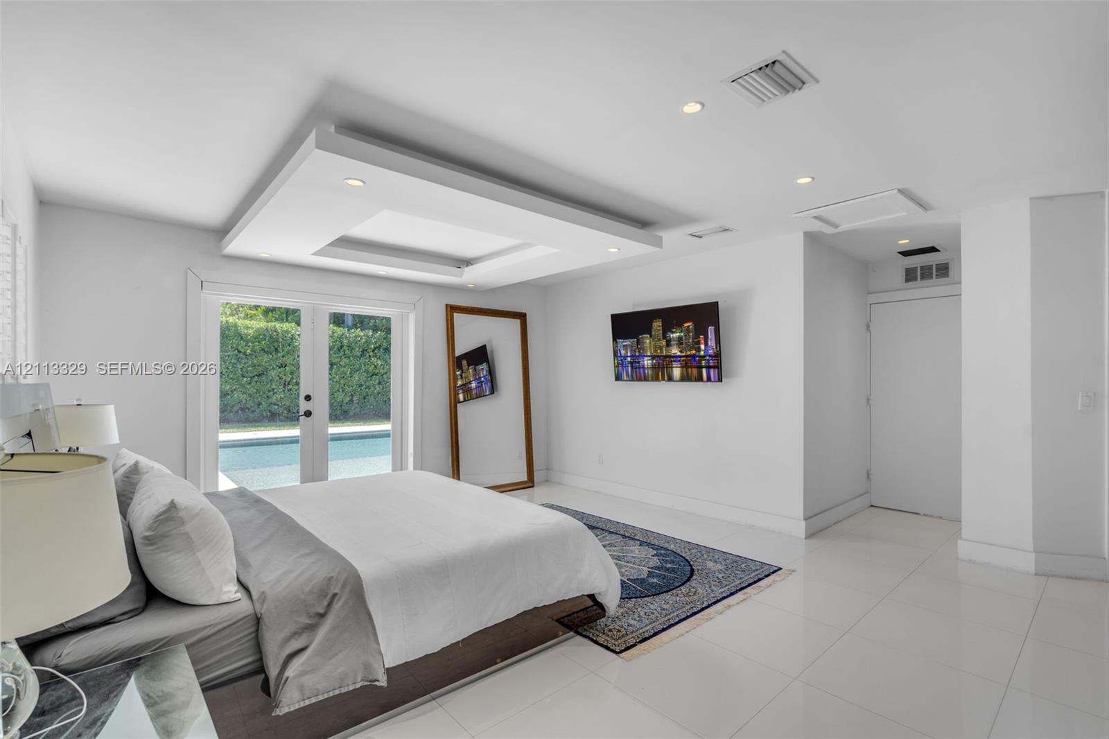 Tray ceiling with recessed lighting, tile flooring, and glass-paneled double doors providing outdoor access