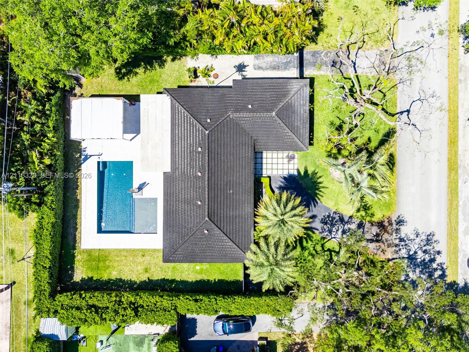 Aerial perspective of a property featuring a dark-tiled roof, a rectangular swimming pool, concrete patio space, and mature landscaping