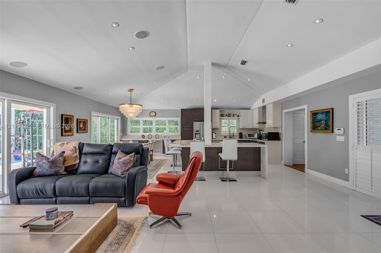 Open-concept interior featuring vaulted ceilings with recessed lighting, high-gloss tile flooring, a tiered kitchen island with quartz countertops, and a tiered crystal chandelier