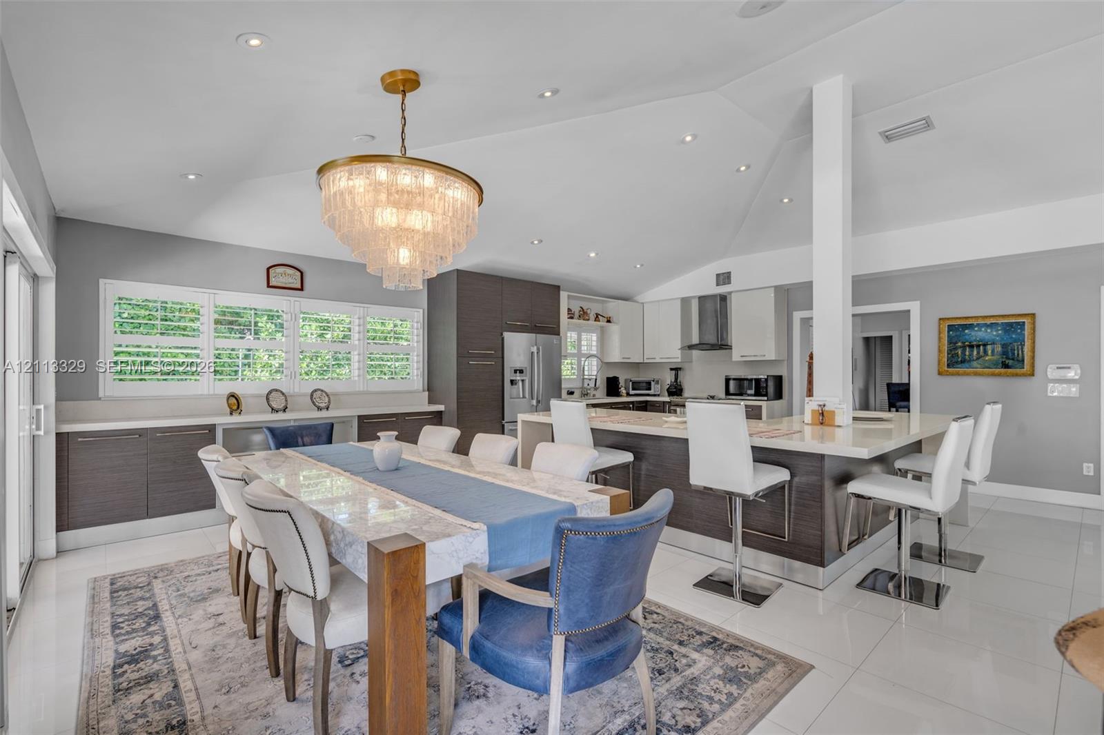 Open-concept kitchen and dining area featuring a vaulted ceiling, recessed lighting, multi-tone custom cabinetry, a stone-surfaced kitchen island, and polished tile flooring