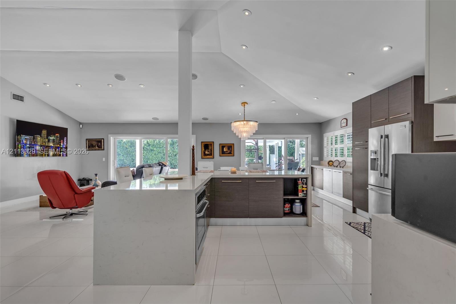 Open-concept kitchen featuring an oversized island with a solid surface countertop, flat-panel cabinetry, recessed ceiling lighting, and porcelain tile flooring