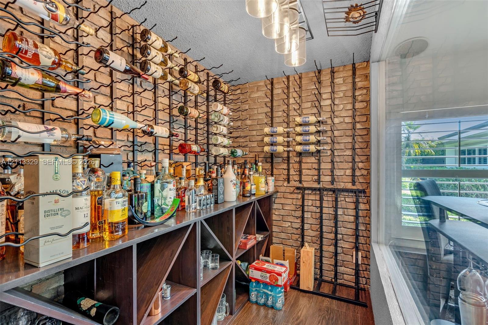 Custom beverage storage space featuring a full-wall brick accent, integrated floor-to-ceiling metal racking, built-in wooden shelving with geometric cubbies, and overhead glass pendant lighting