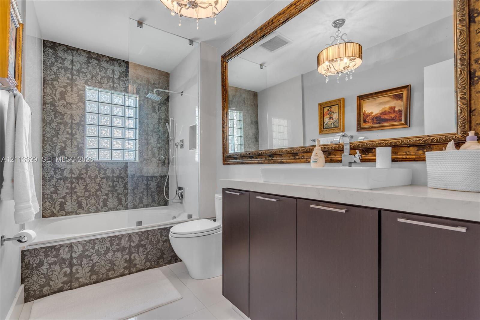 Bathroom featuring a floating vanity with a vessel sink, stone-finish countertop, glass-enclosed shower with a glass block window, and large-format tile surround