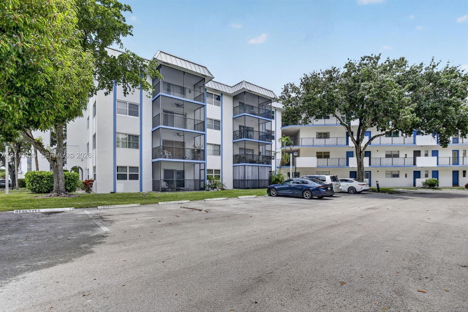 Multi-story building exterior featuring screened-in balconies, metal roof accents, and mature landscaping Multi-story building exterior featuring screened-in balconies, metal roof accents, and mature landscaping