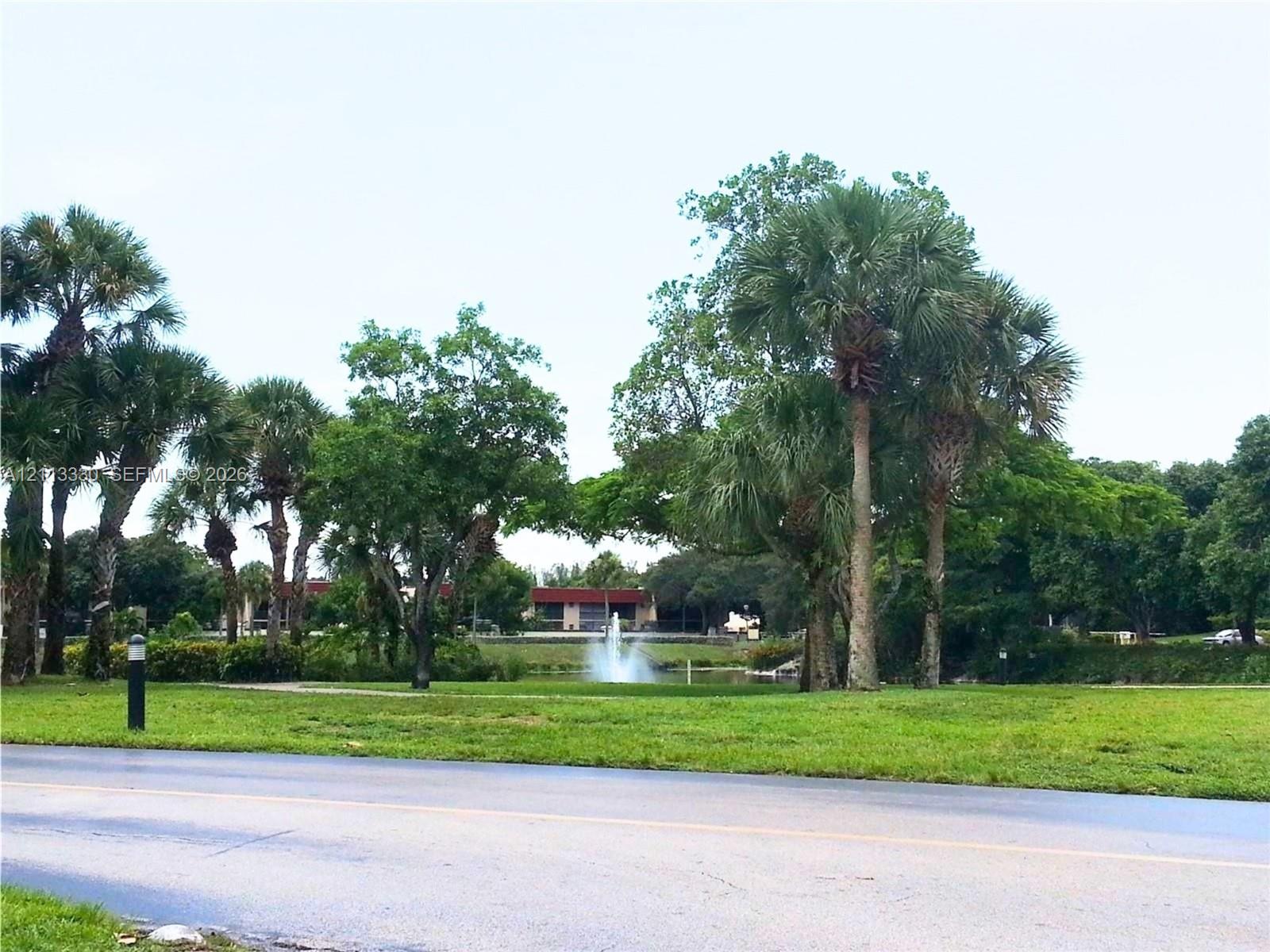 Grounds featuring mature palm trees, sprawling lawn, pond with fountain, and paved path Grounds featuring mature palm trees, sprawling lawn, pond with fountain, and paved path