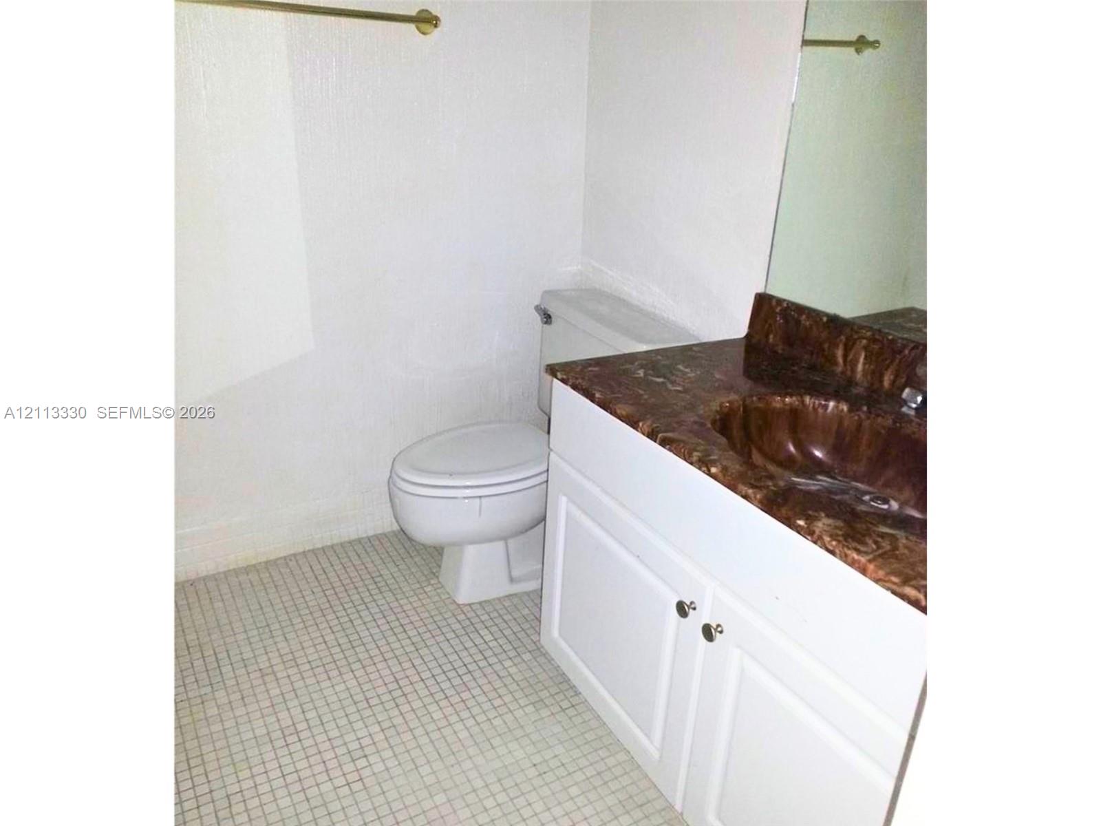 White vanity cabinet with a stone-finish countertop and integrated sink, paired with small-format tile flooring and a wall-mounted mirror White vanity cabinet with a stone-finish countertop and integrated sink, paired with small-format tile flooring and a wall-mounted mirror