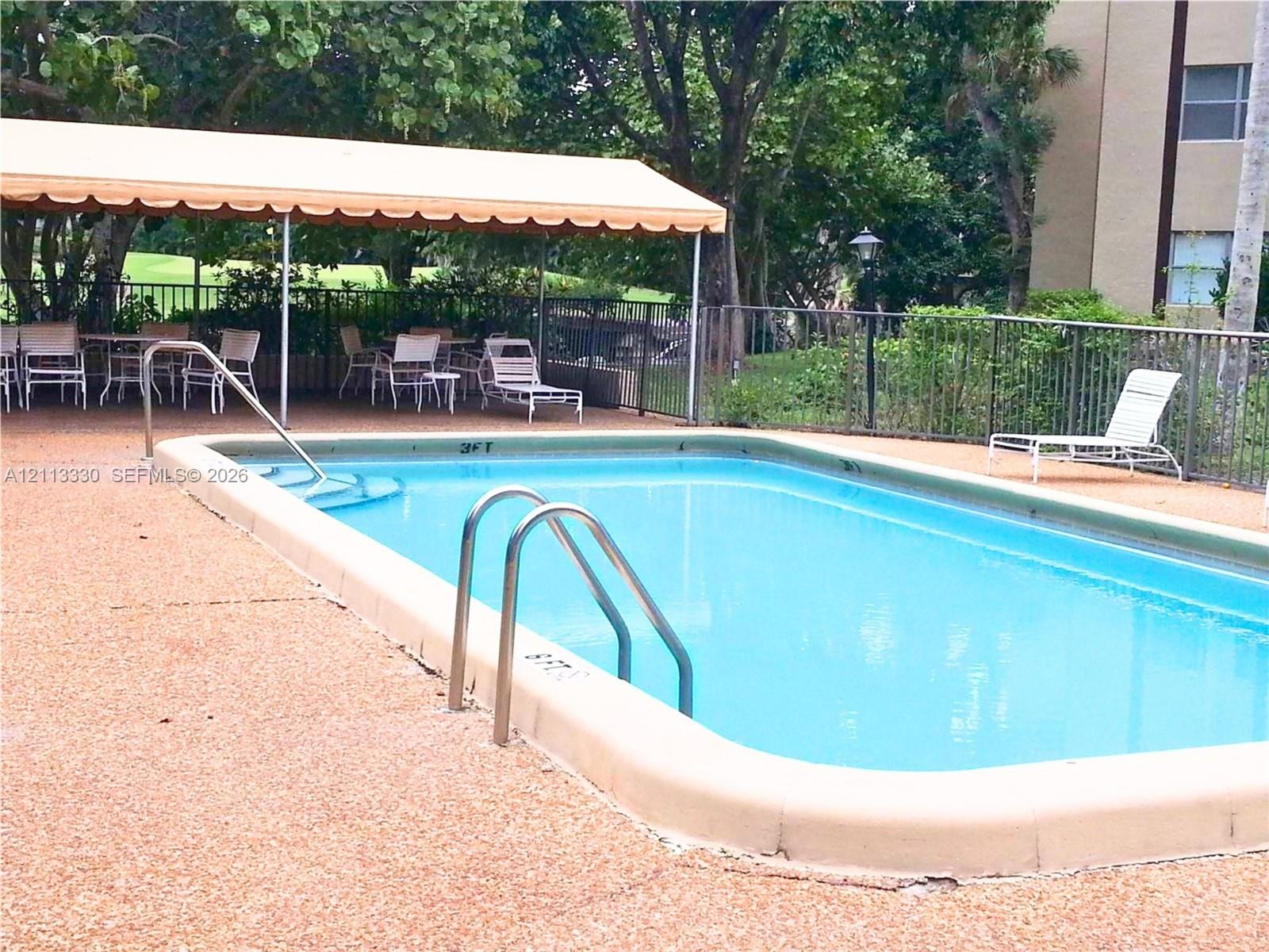 Inground swimming pool with metal ladder and integrated steps, concrete deck, and overhead canopy