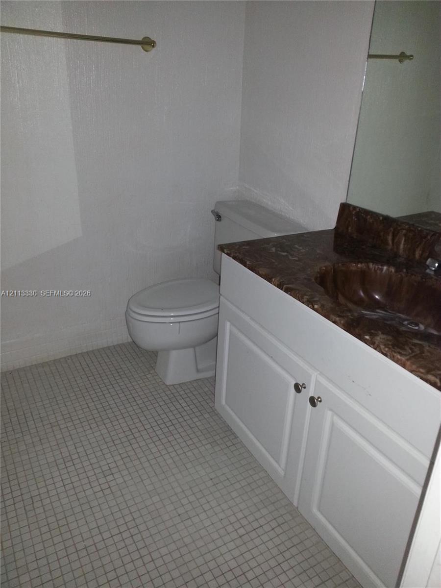 Vanity featuring a stone-look countertop with an integrated basin, white shaker-style cabinetry, a large wall-mounted mirror, and tile flooring Vanity featuring a stone-look countertop with an integrated basin, white shaker-style cabinetry, a large wall-mounted mirror, and tile flooring