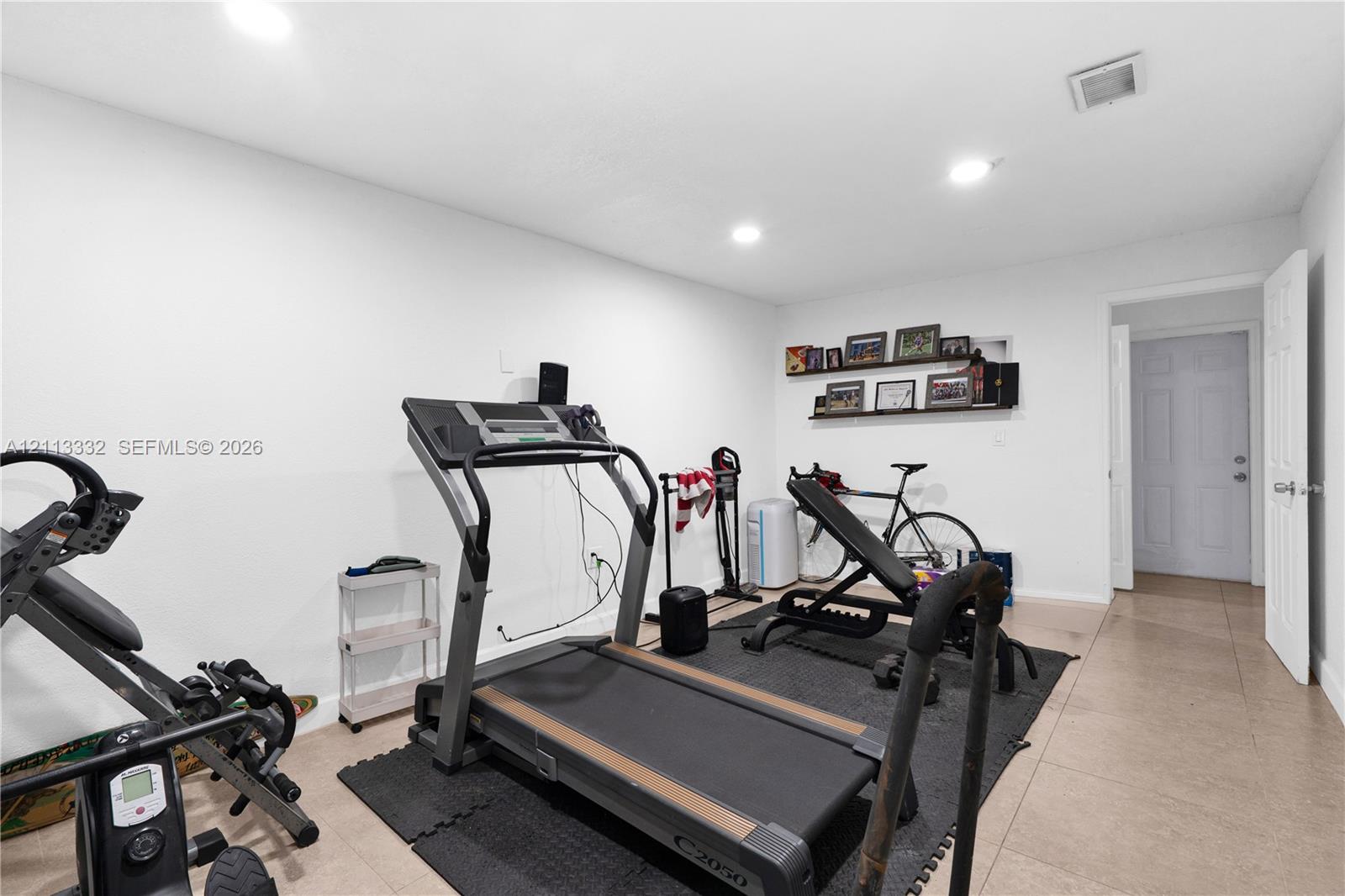 Neutral interior space featuring large-format ceramic tile flooring, recessed ceiling lighting, a built-in wall niche with shelving, and a six-panel interior door