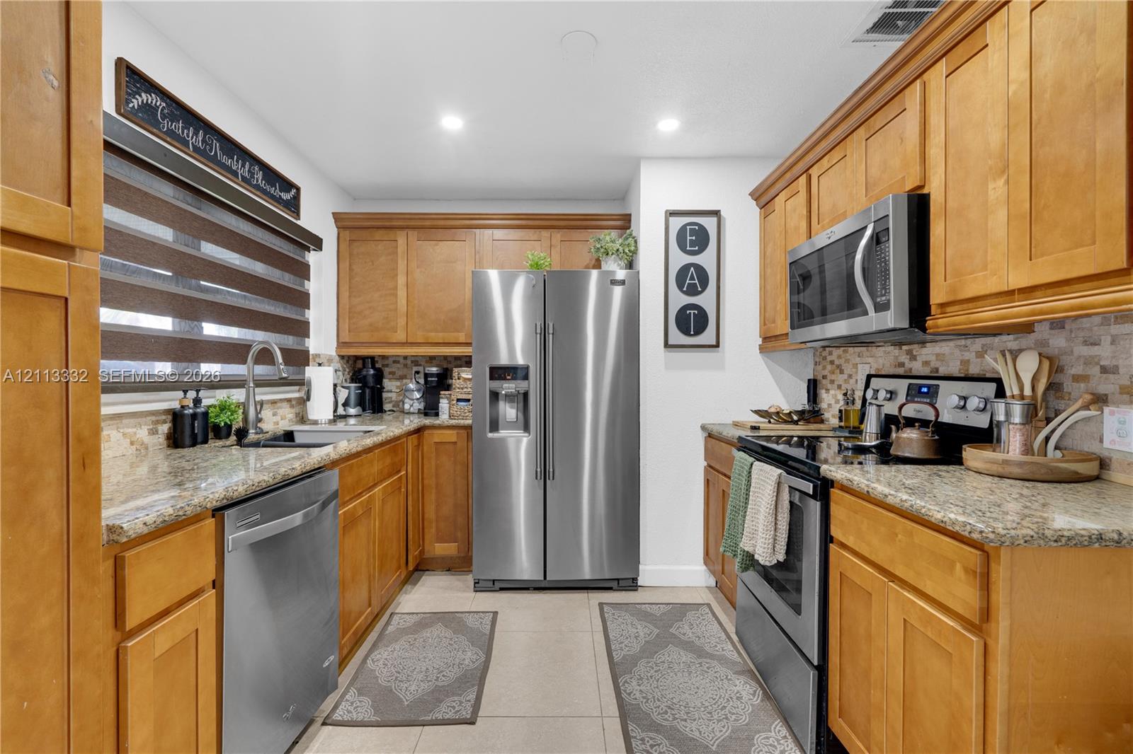 Kitchen featuring honey-toned wood cabinetry, stone countertops, mosaic tile backsplash, stainless steel appliances, and recessed lighting