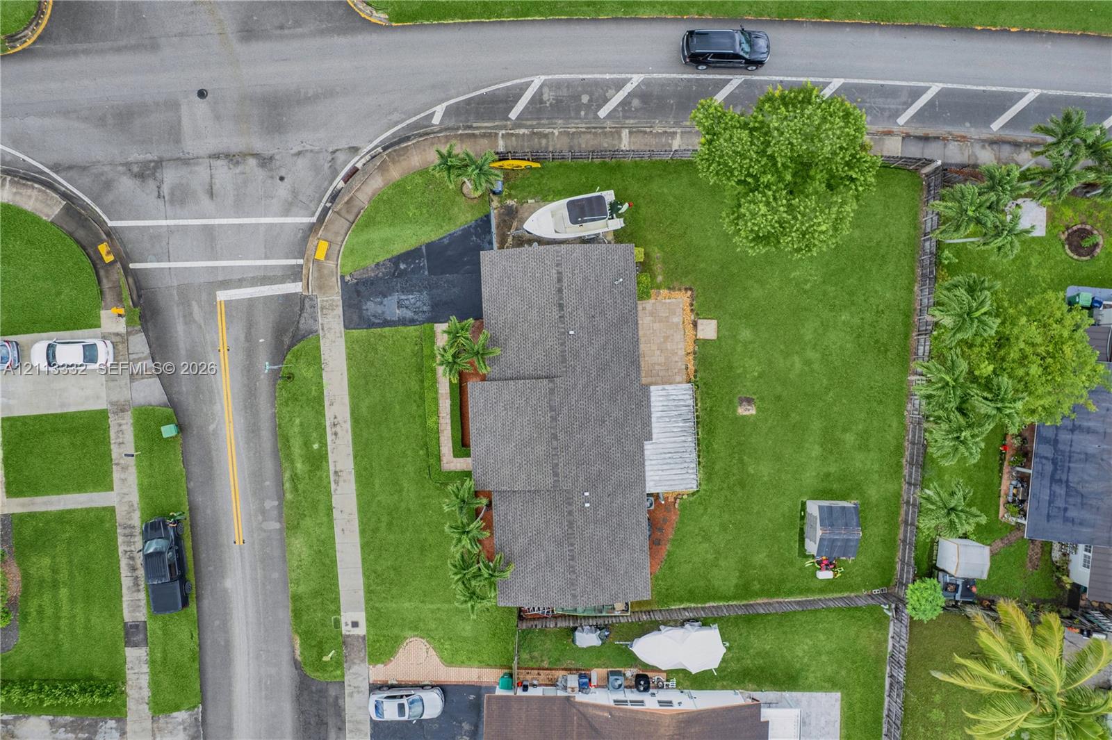 Aerial perspective of a property featuring an asphalt driveway, a paved patio area, a fenced-in lawn, and mature landscaping