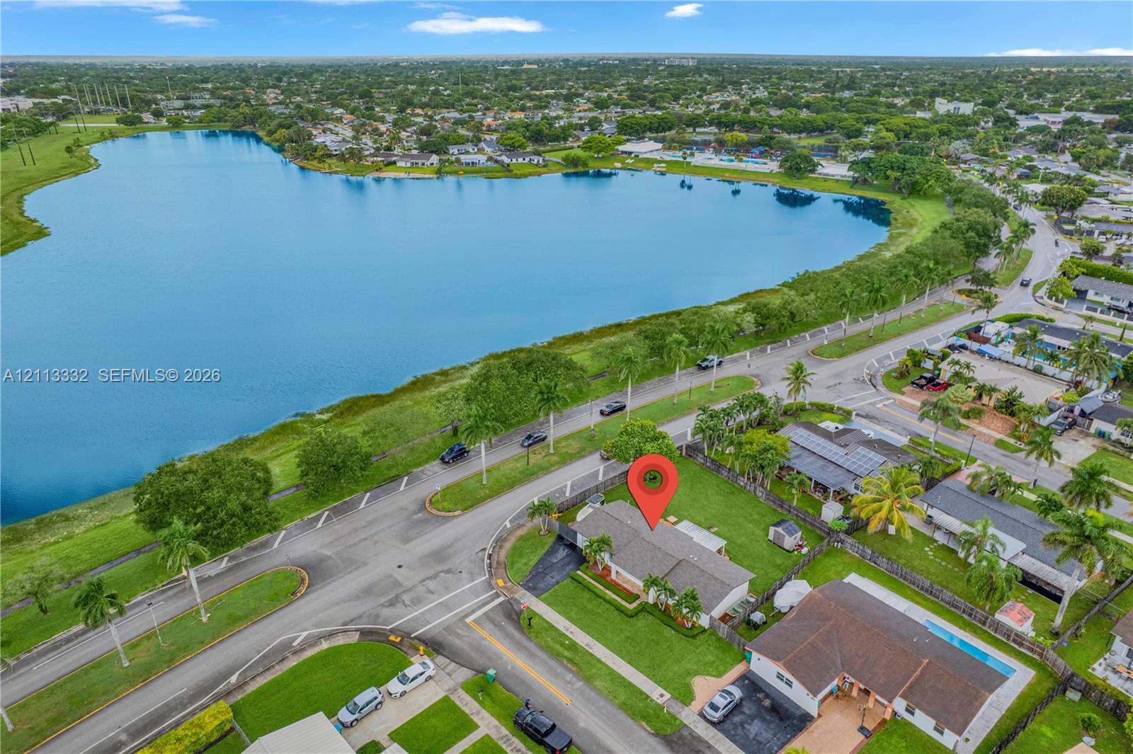 Aerial perspective of residential property featuring a pitched roof, asphalt driveway, and manicured lawn, situated in proximity to a large waterfront