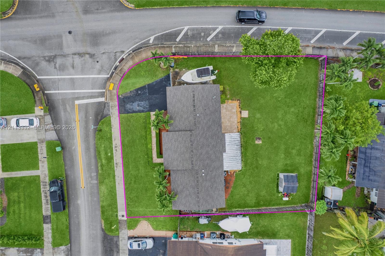 Corner lot featuring a large lawn, paved driveway, stone patio, and detached storage structure