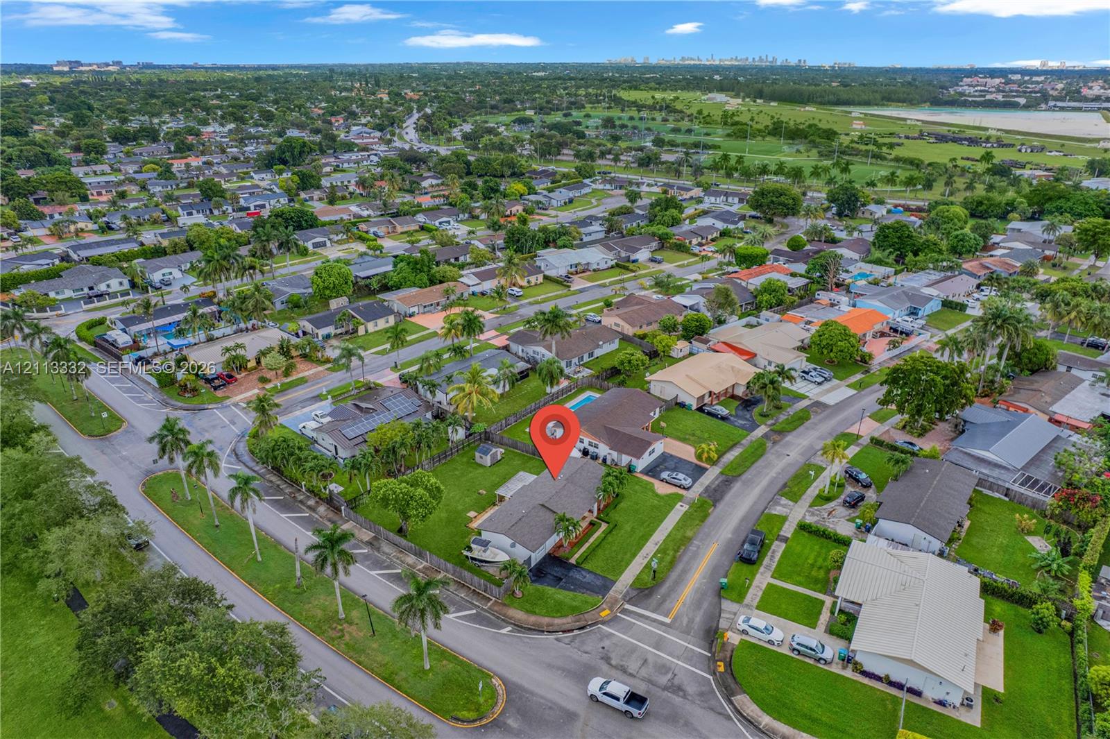 Aerial perspective of corner lot featuring a fenced backyard, private swimming pool, mature palm trees, and asphalt driveway