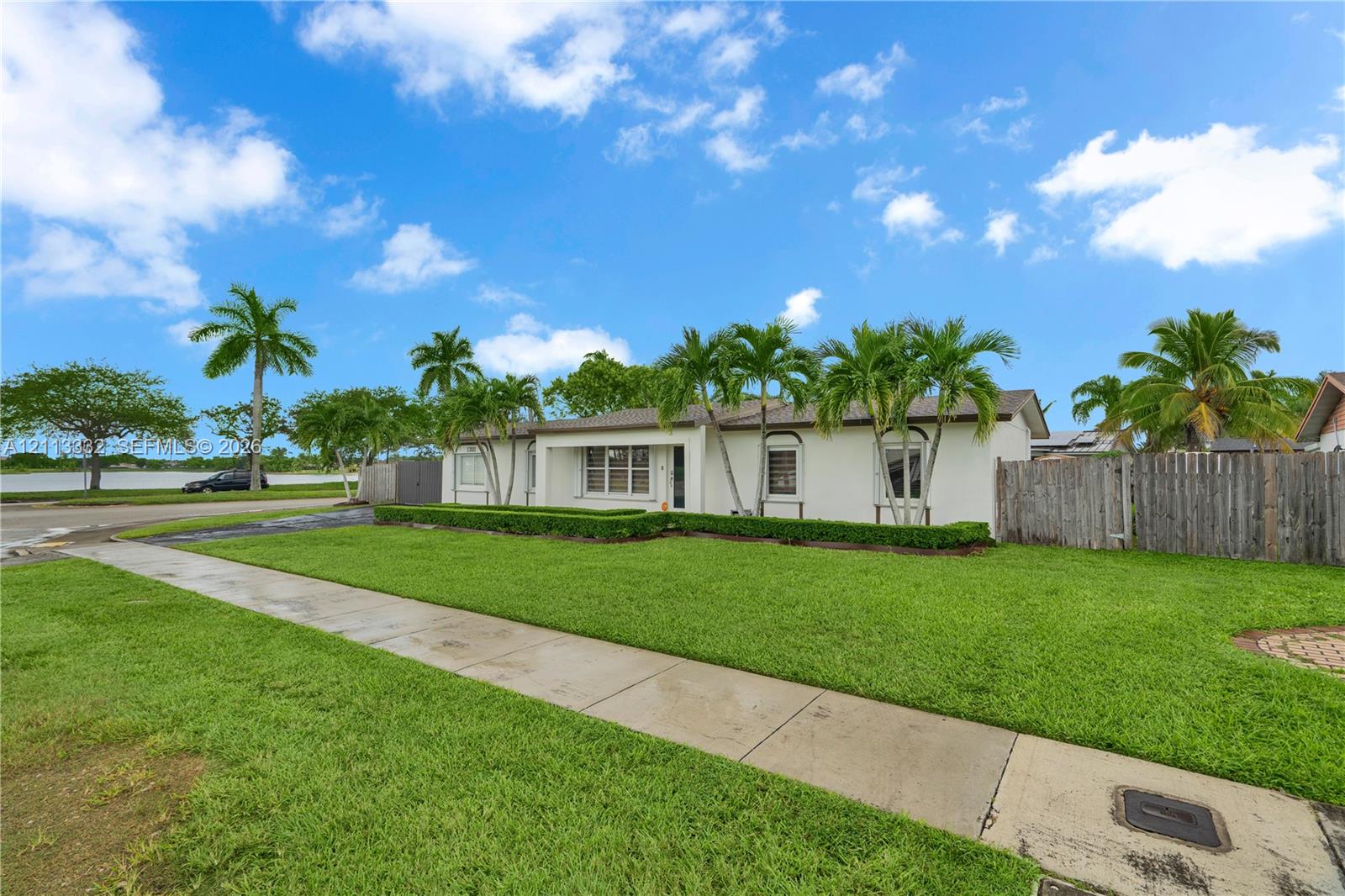 Single-story residence featuring a smooth stucco exterior, manicured lawn, established landscaping, and a wood privacy fence