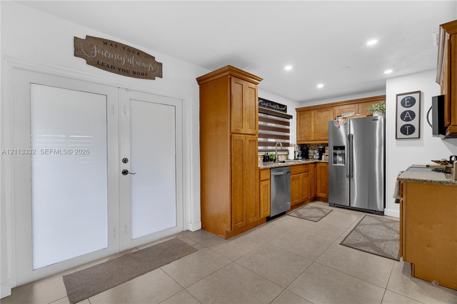 Kitchen featuring shaker-style cabinetry, stainless steel appliances, stone-surface countertops, tile flooring, and dual glass-panel entry doors