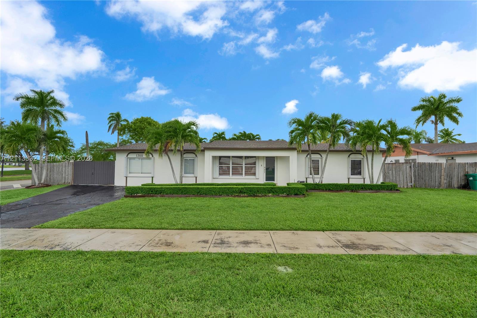 Single-story exterior featuring light-toned stucco, a multi-pane front window, manicured shrubbery, and mature palm trees across the front lawn
