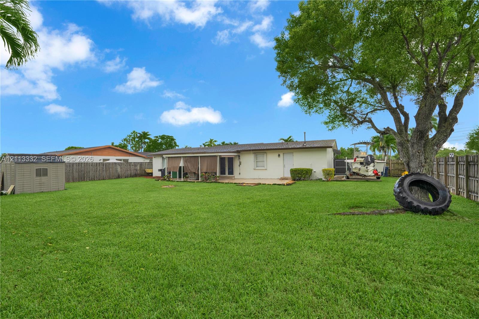 Expansive backyard featuring a large grass lawn, perimeter wood fencing, a detached resin storage shed, and a mature shade tree