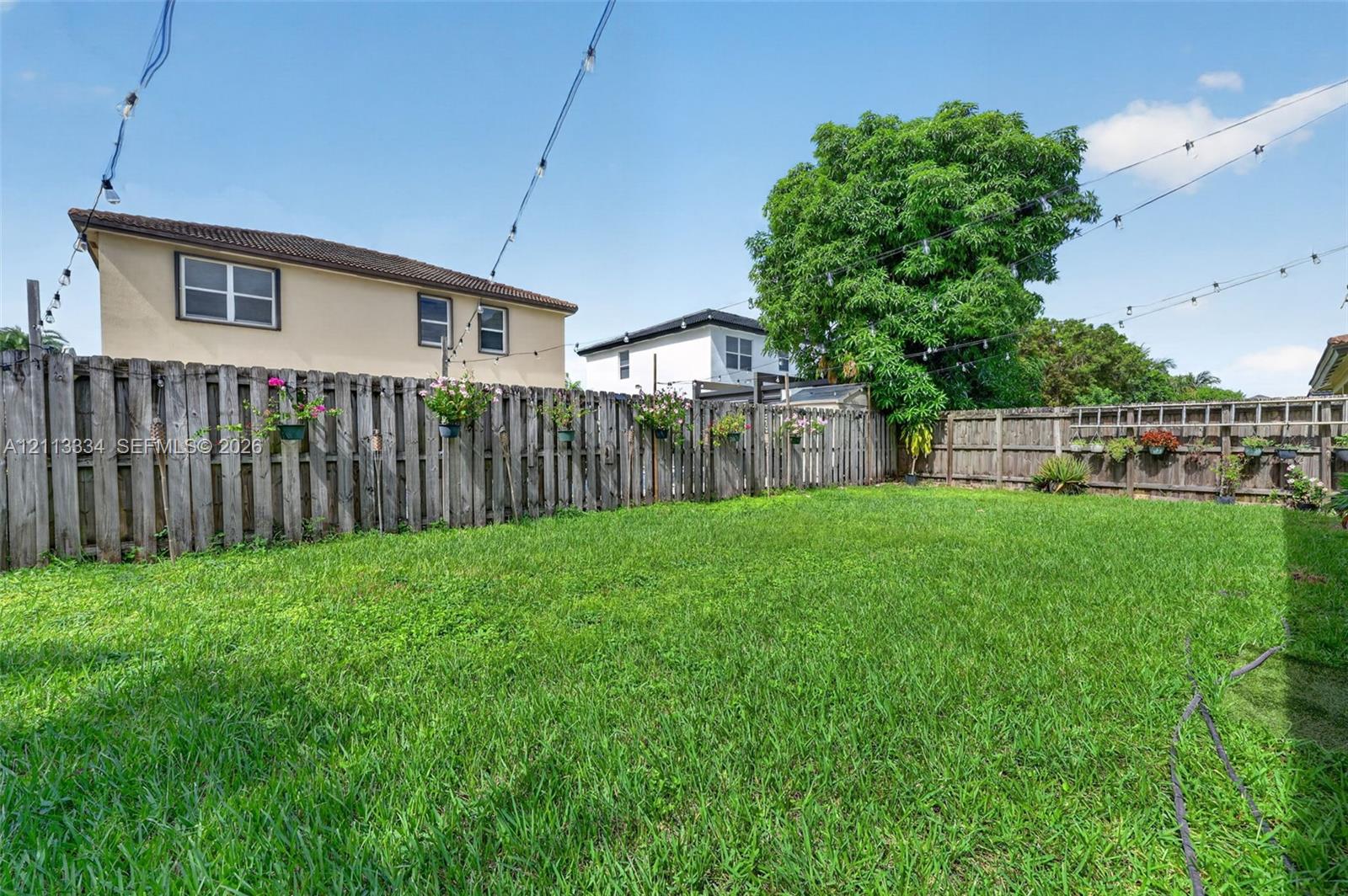 Expansive backyard featuring a manicured lawn, full-perimeter wood privacy fencing, and overhead string lighting
