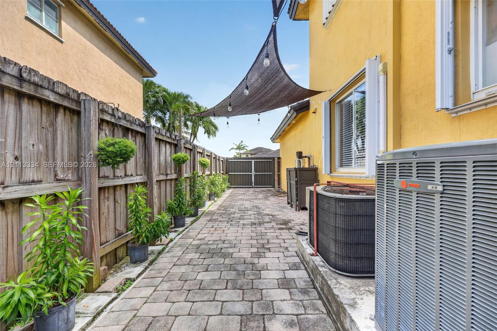Side yard featuring paver flooring, wood-panel fencing, and a retractable overhead sun shade