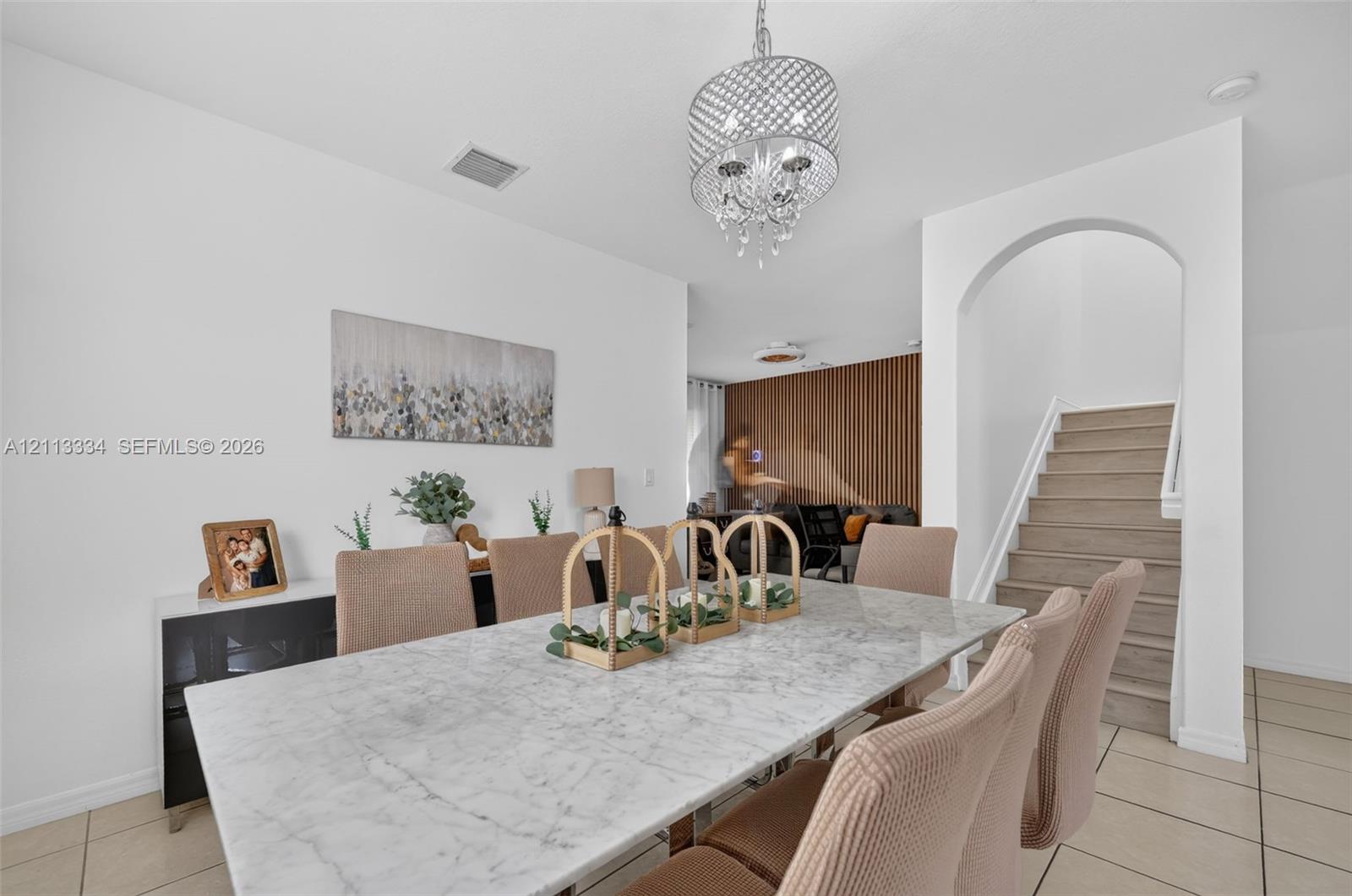 Open-concept dining area featuring a tiered crystal chandelier, tile flooring, an arched entryway, and a vertical wood-slat accent wall