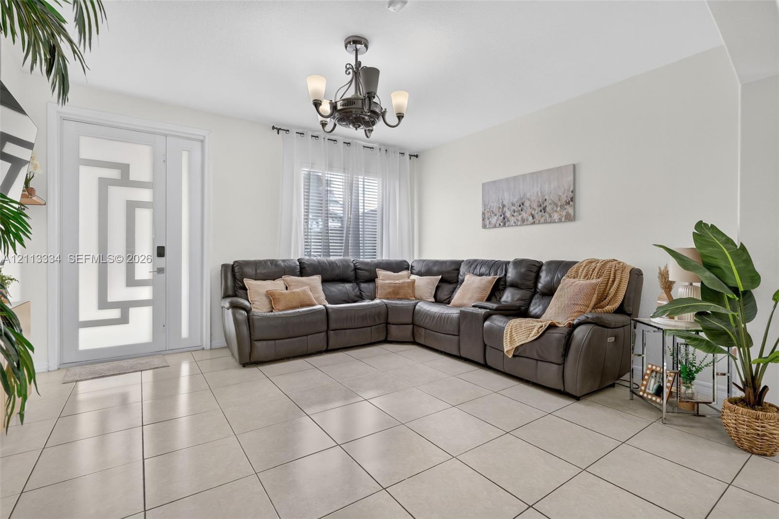 Neutral tile flooring, decorative front door with geometric glass inlay, and five-arm transitional chandelier